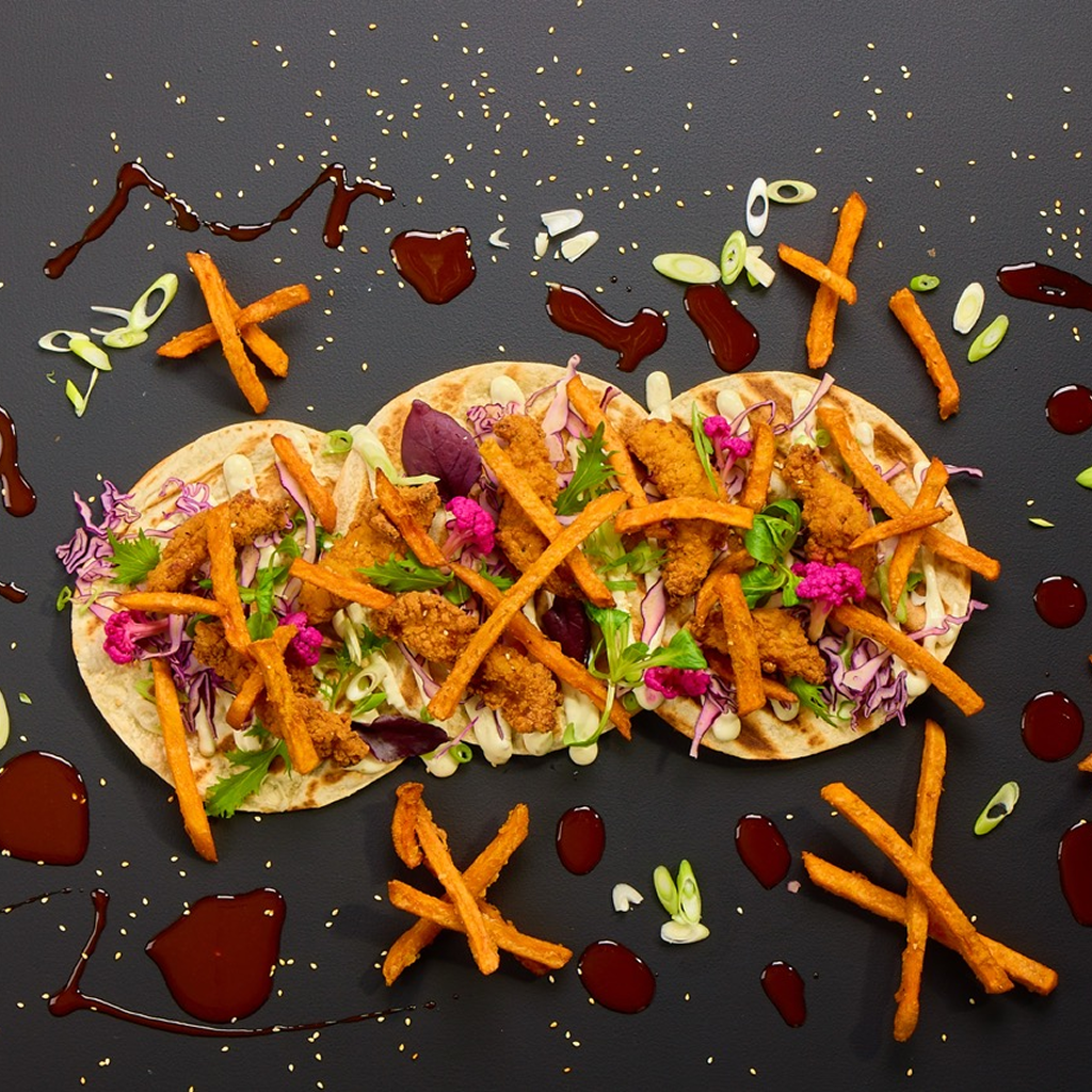 Tortilla-Wrap mit gebackenen Chicken Stripes, Rotkohl, Weißkohl, Süßkartoffelpommes, Jalapeño Lime Dip, Korean Dak Gangjeong Sauce, Frühlingslauch und Sesam.